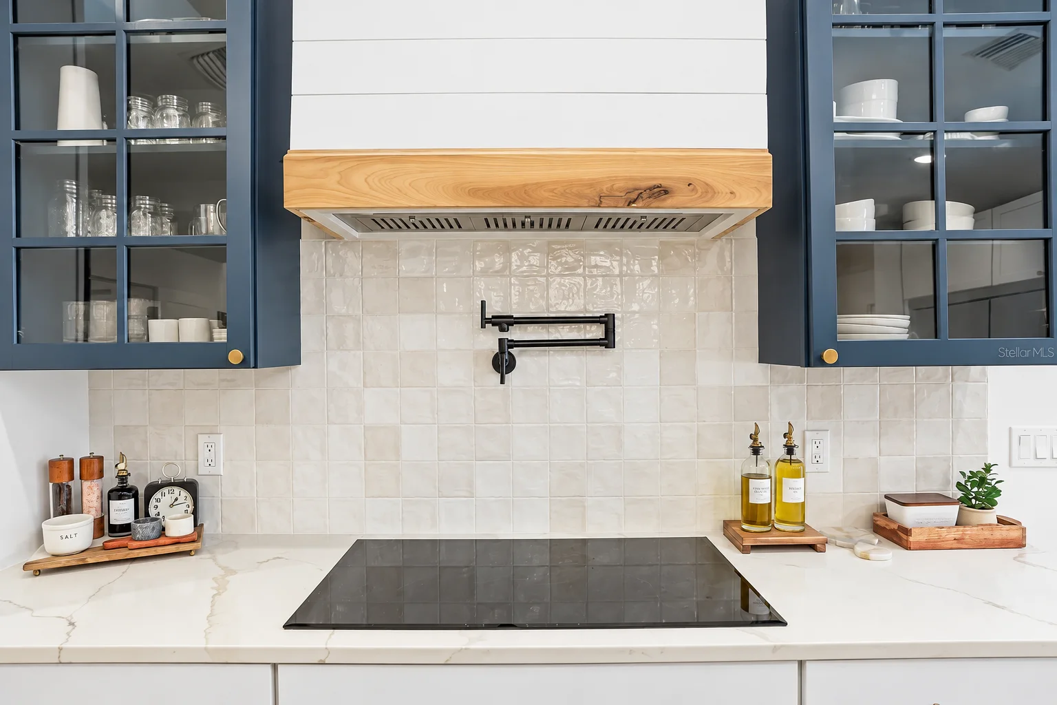 Navy glass front uppers and wood hood with pot filler over the cooktop, Sarasota kitchen remodel