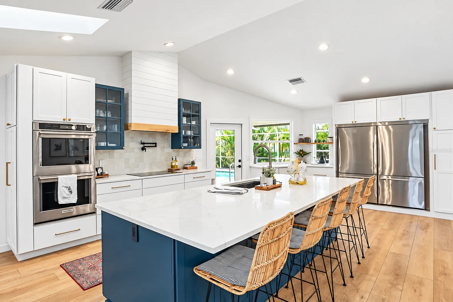 Wall ovens and stainless fridge beside the navy island under a skylight, Sarasota remodel